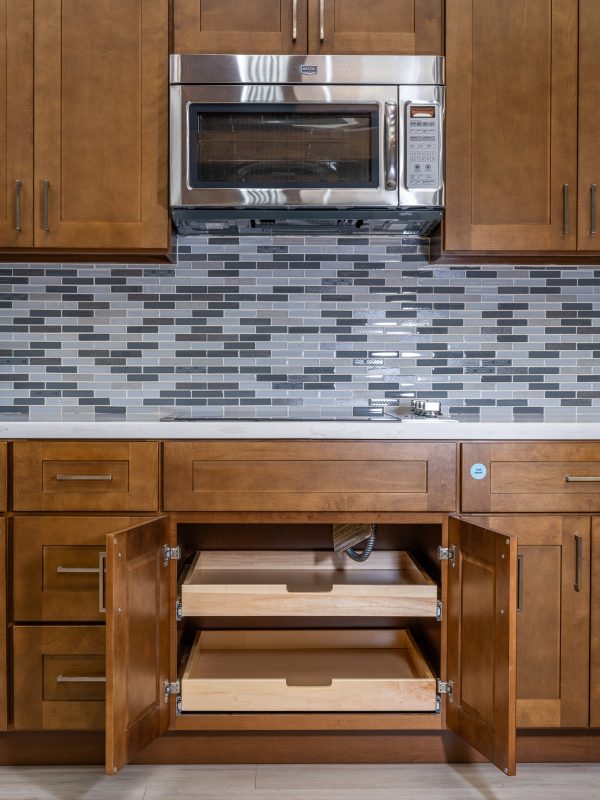 Complete kitchen view with wooden cabinetry, gray subway tile backsplash, stainless steel microwave, and open pull-out drawers below