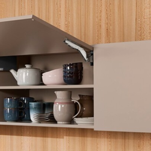 Beige wall-mounted cabinet with hinged door open displaying white teapot and ceramic dishware on shelves
