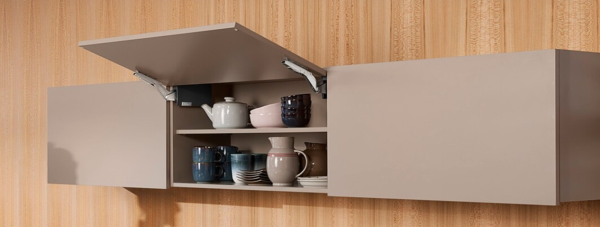 Beige wall-mounted cabinet with hinged door open displaying white teapot and ceramic dishware on shelves