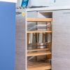 Kitchen cabinet interior showing wooden shelves with metal containers and silver organizational dividers