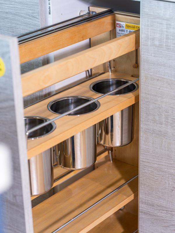Close-up of wooden pull-out drawer with three circular stainless steel pot holders and multiple shelf levels