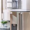 Modern kitchen cabinet with pull-out wire shelving, stainless steel refrigerator and dark countertop