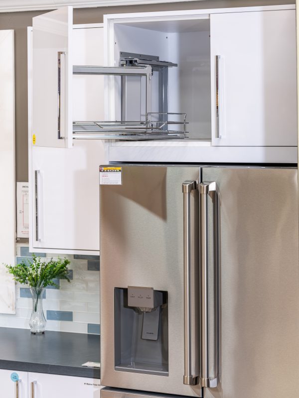 Modern kitchen cabinet with pull-out wire shelving, stainless steel refrigerator and dark countertop