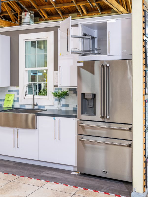 Modern kitchen display with white cabinetry, stainless steel refrigerator, farmhouse sink and blue subway tile backsplash