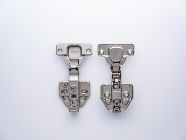 Comparison of two stainless steel cabinet hinges with DTC branding, showing front-facing views with adjustment mechanisms