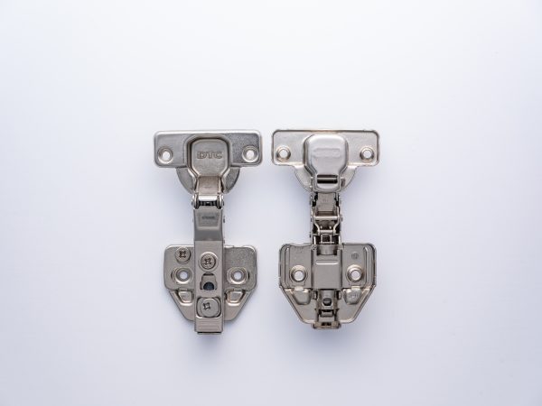 Two stainless steel cabinet hinges shown front and back views, displaying DTC branding and mounting holes