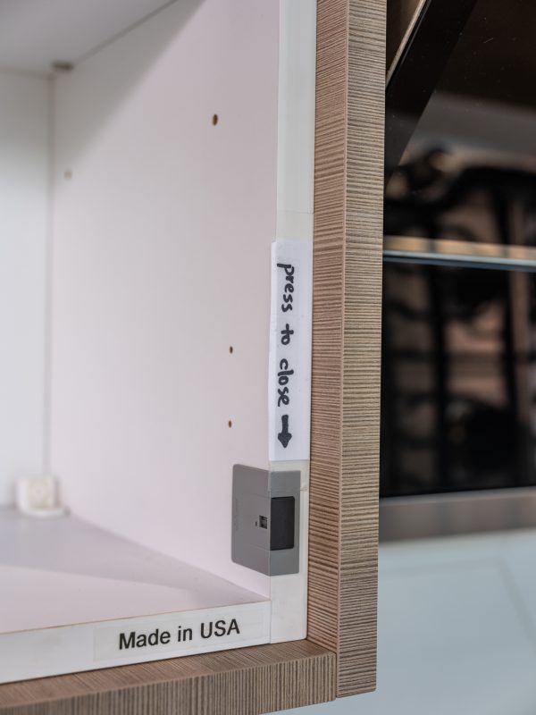 Close-up of cabinet side panel showing 'press to close' label with downward arrow and 'Made in USA' text, with gray electronic mechanism visible