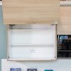 Light wood cabinet with closed upper door and open lower shelves displaying white interior, with caution and product information signs below