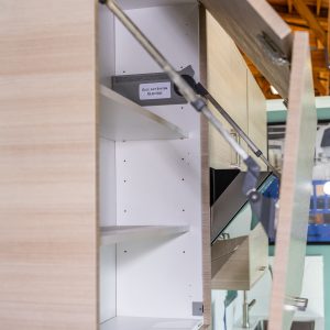 Interior view of open wooden cabinet with white shelves and metal support rod, showing 'Exc-Lift System Electric' label inside