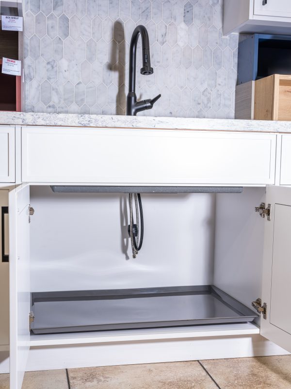 Under-sink cabinet interior with gray pull-out storage tray and plumbing connections visible