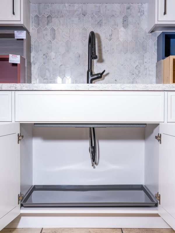 Kitchen sink cabinet with gray pull-out tray beneath marble hexagonal tile backsplash and black faucet