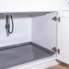 Open white kitchen cabinet with gray pull-out tray and stainless steel hinges, showing interior storage space and coiled black hose
