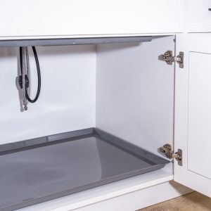 Open white kitchen cabinet with gray pull-out tray and stainless steel hinges, showing interior storage space and coiled black hose