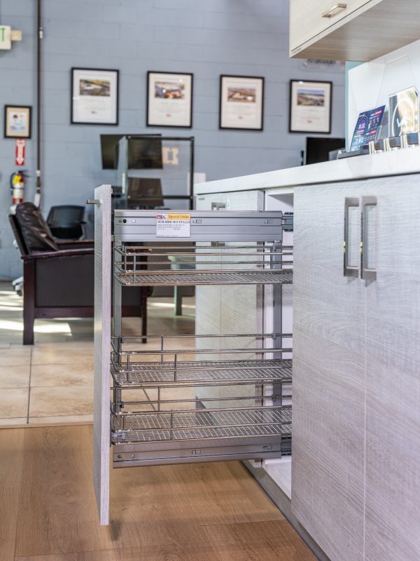 Pull-out wire basket organizer mounted inside cabinet with multiple shelves in contemporary kitchen showroom