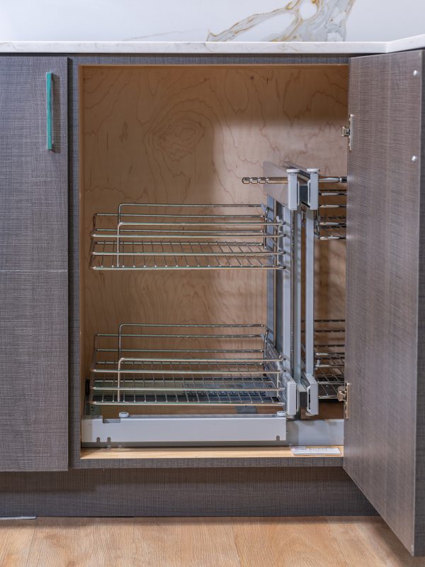 Interior view of kitchen cabinet with extended pull-out wire basket storage system displaying three-tier chrome shelving for corner cabinet organization