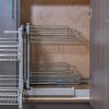 Kitchen cabinet interior with pull-out wire basket organizer system showing two-tier chrome shelving mounted inside closed cabinet doors