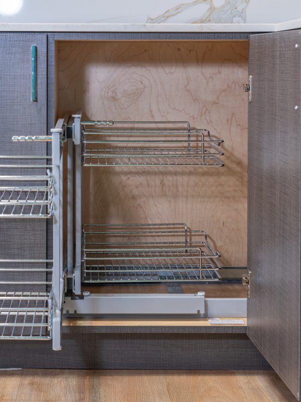 Kitchen cabinet interior with pull-out wire basket organizer system showing two-tier chrome shelving mounted inside closed cabinet doors