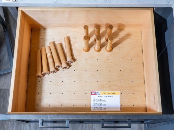 Open kitchen drawer displaying wooden peg board organizer with rolling pins and utensils