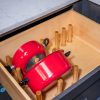 Wooden kitchen drawer organizer containing two red cookpots with lids and wooden dividers for utensil storage