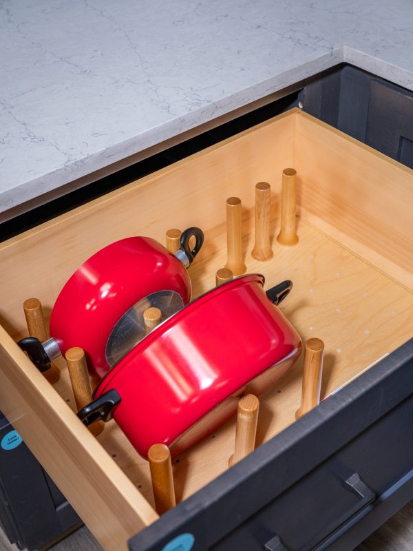 Wooden kitchen drawer organizer containing two red cookpots with lids and wooden dividers for utensil storage