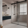 Modern bathroom with black framed glass shower enclosure, white tile walls, circular illuminated mirror, dark blue vanity cabinet, and window with blinds