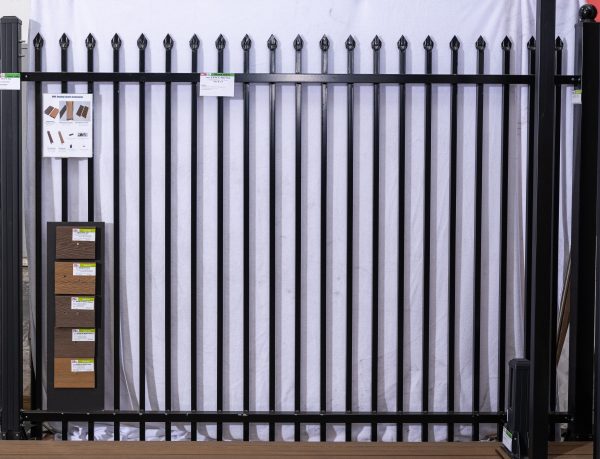 Black ornamental fence display showing multiple pickets with spear-point finials and wood grain finish samples