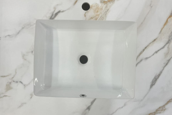 White rectangular ceramic undermount sink with overflow hole and faucet mounting hole, viewed from above on marble surface